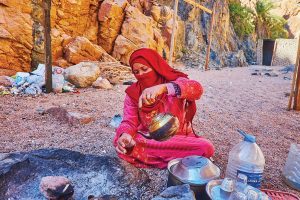 المرأة البدوية المضيافة في الزي التقليدي والنقاب تعد الشاي الساخن المغلي على الفحم